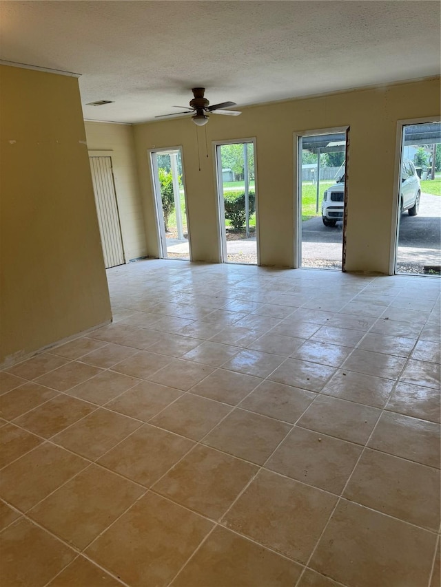 empty room with a textured ceiling, ceiling fan, plenty of natural light, and visible vents