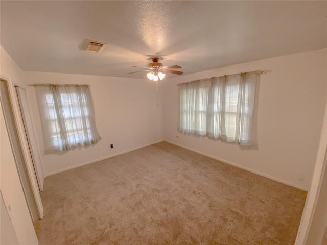 unfurnished room with light carpet, baseboards, visible vents, and a ceiling fan