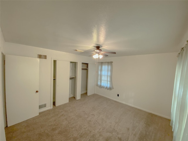 unfurnished bedroom with light carpet, a ceiling fan, visible vents, and multiple closets