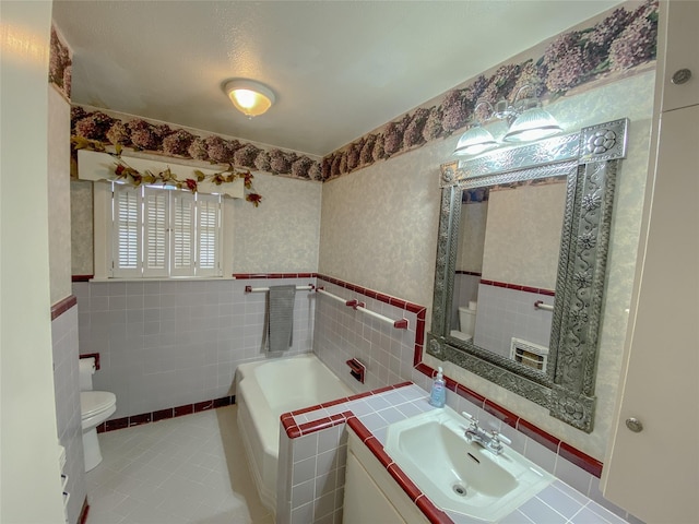 full bathroom with wallpapered walls, toilet, tile patterned flooring, vanity, and tile walls