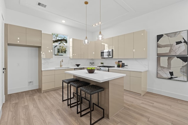 kitchen featuring sink, stainless steel appliances, cream cabinets, decorative light fixtures, and a kitchen island