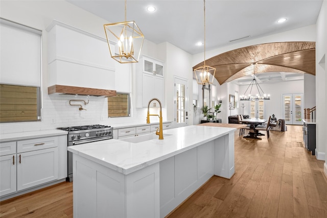 kitchen featuring decorative light fixtures, sink, high end stainless steel range oven, and an island with sink