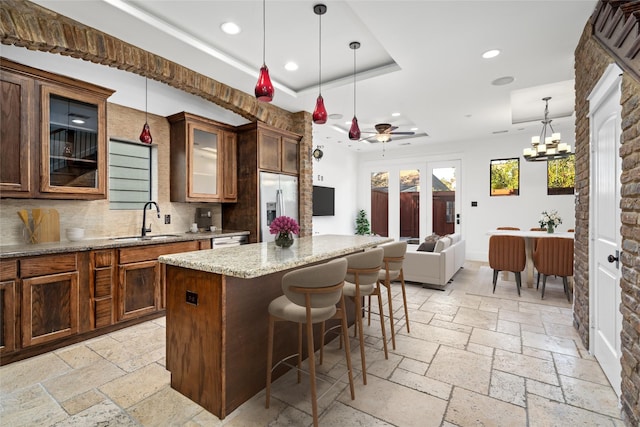 kitchen featuring sink, hanging light fixtures, light stone counters, a kitchen island, and appliances with stainless steel finishes