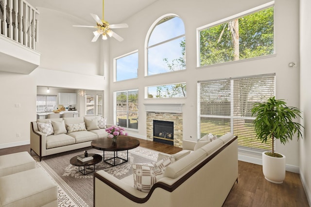 living room featuring a high ceiling, dark hardwood / wood-style flooring, a stone fireplace, and ceiling fan