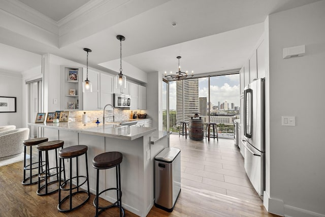 kitchen featuring backsplash, kitchen peninsula, decorative light fixtures, white cabinets, and appliances with stainless steel finishes