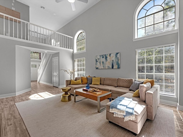 living room with ceiling fan, light wood-type flooring, and a towering ceiling