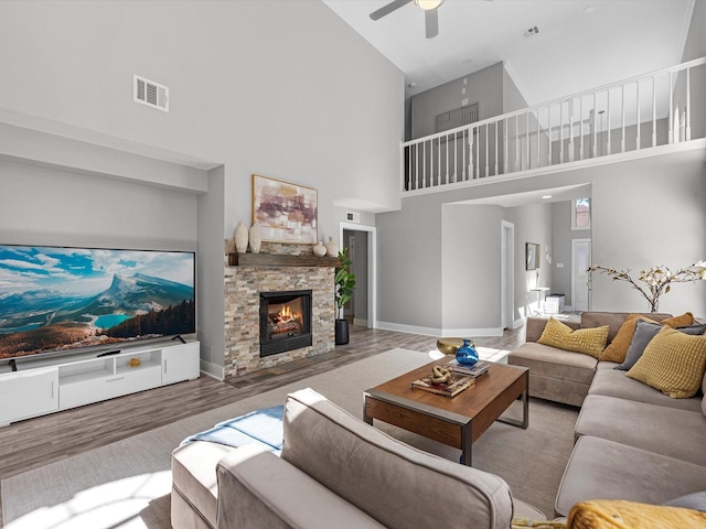 living room featuring a stone fireplace, ceiling fan, a high ceiling, and hardwood / wood-style flooring