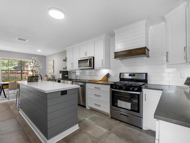 kitchen with custom exhaust hood, appliances with stainless steel finishes, tasteful backsplash, a kitchen island, and white cabinetry