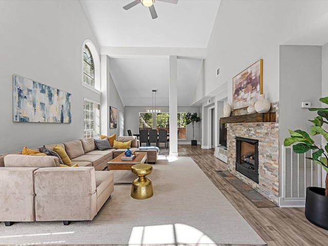 living room featuring ceiling fan with notable chandelier, a stone fireplace, wood-type flooring, and high vaulted ceiling