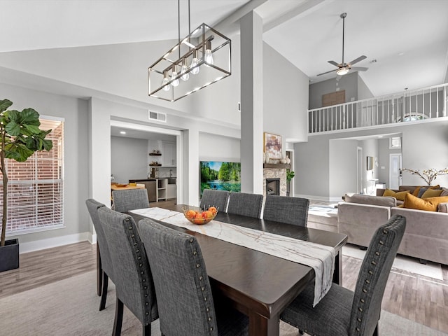 dining room featuring ceiling fan, a fireplace, high vaulted ceiling, and light hardwood / wood-style flooring