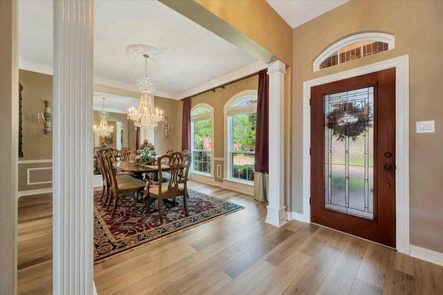 foyer with ornate columns, crown molding, a chandelier, and light wood-type flooring