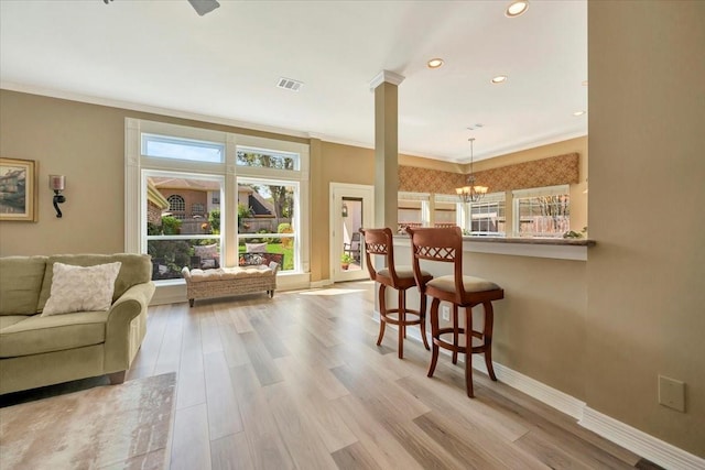 interior space featuring light wood-type flooring, crown molding, a notable chandelier, and ornate columns