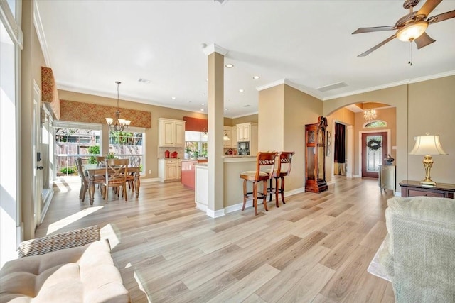 living room with ceiling fan with notable chandelier, crown molding, and light hardwood / wood-style flooring