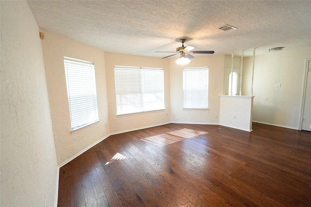 empty room with a textured ceiling, plenty of natural light, ceiling fan, and dark wood-type flooring