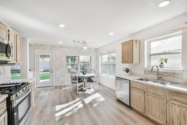 kitchen with light brown cabinetry, light wood-type flooring, stainless steel appliances, ceiling fan, and sink