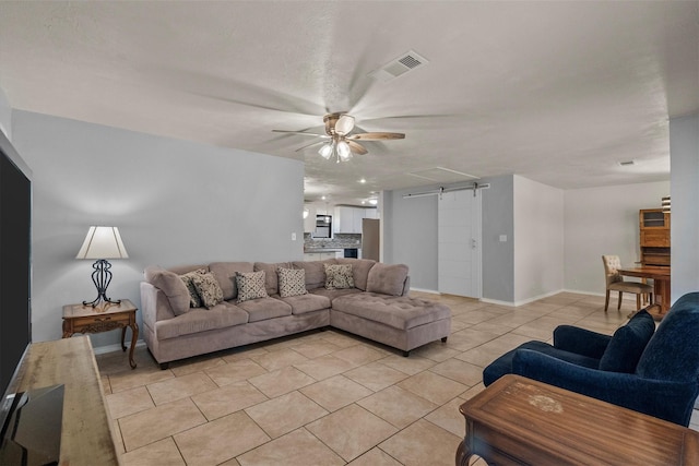 living area featuring light tile patterned floors, a barn door, visible vents, baseboards, and a ceiling fan