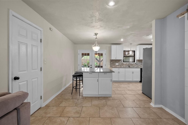 kitchen with freestanding refrigerator, french doors, a kitchen bar, white cabinetry, and a sink