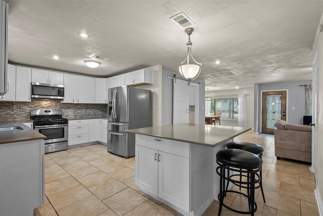 kitchen with stainless steel appliances, pendant lighting, white cabinets, and open floor plan