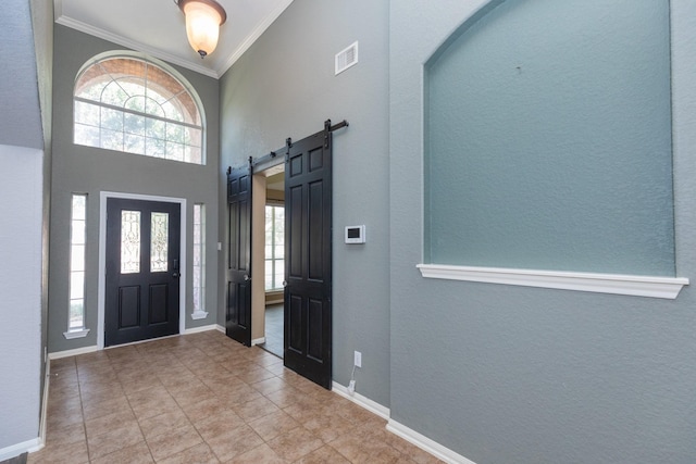 foyer featuring a barn door, a healthy amount of sunlight, crown molding, and a high ceiling