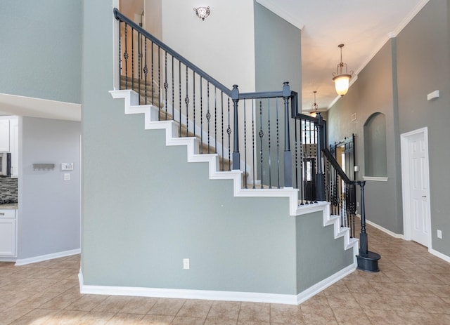 stairway featuring tile patterned floors, an inviting chandelier, a high ceiling, and ornamental molding