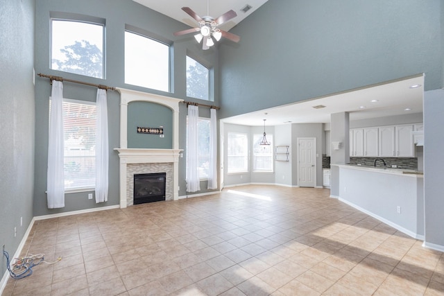 unfurnished living room featuring ceiling fan, a stone fireplace, light tile patterned floors, and a high ceiling