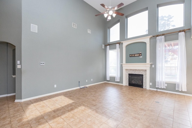 unfurnished living room with a fireplace, a high ceiling, light tile patterned floors, and ceiling fan