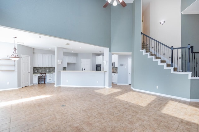 unfurnished living room featuring ceiling fan, a towering ceiling, and light tile patterned flooring