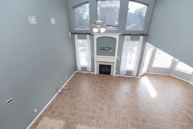 unfurnished living room with ceiling fan, a stone fireplace, and a high ceiling