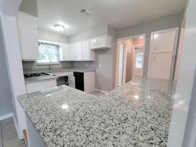 kitchen featuring kitchen peninsula, light stone countertops, black dishwasher, a healthy amount of sunlight, and white cabinetry