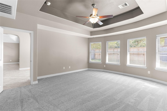 carpeted empty room with a raised ceiling, a wealth of natural light, and ceiling fan