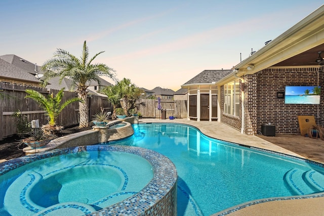 pool at dusk featuring an in ground hot tub and a patio area