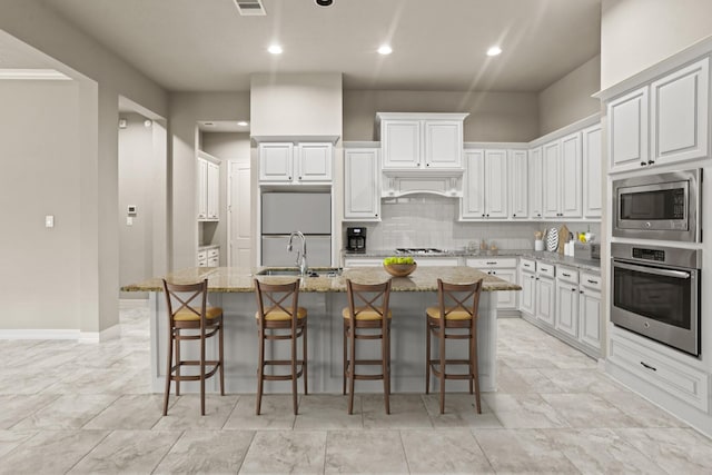 kitchen featuring built in appliances, white cabinetry, a kitchen island with sink, and light stone counters