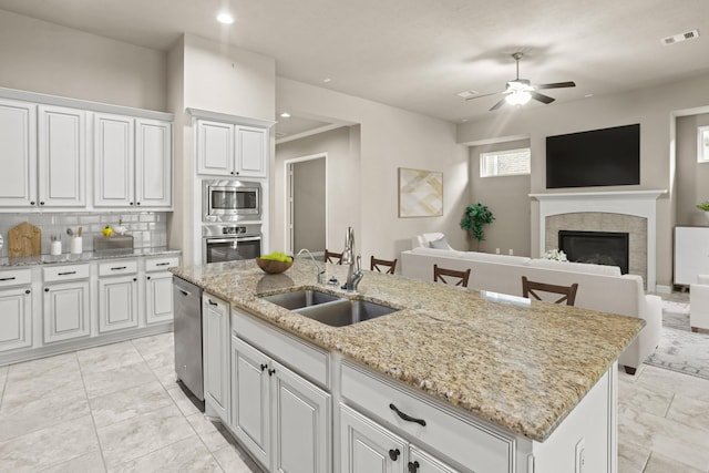 kitchen with a kitchen island with sink, appliances with stainless steel finishes, a tiled fireplace, white cabinets, and sink