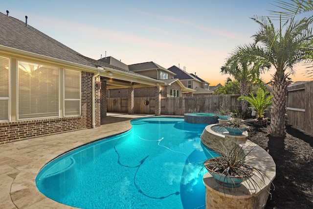 pool at dusk featuring a patio area and an in ground hot tub