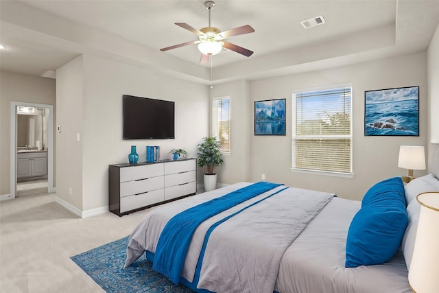 carpeted bedroom with ensuite bathroom, ceiling fan, and a tray ceiling