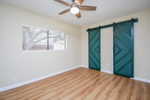 unfurnished bedroom featuring light wood-type flooring, a barn door, and ceiling fan