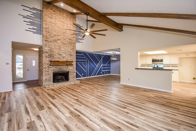 unfurnished living room featuring beam ceiling, ceiling fan, light hardwood / wood-style flooring, high vaulted ceiling, and a fireplace