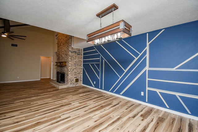 unfurnished living room featuring wood-type flooring, a textured ceiling, a brick fireplace, and ceiling fan