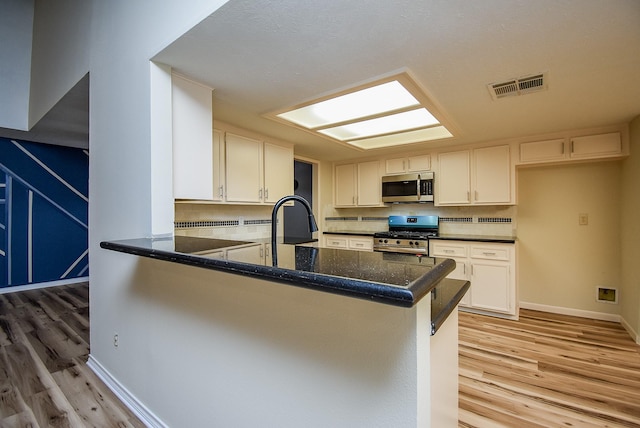 kitchen featuring kitchen peninsula, white cabinets, light wood-type flooring, and appliances with stainless steel finishes