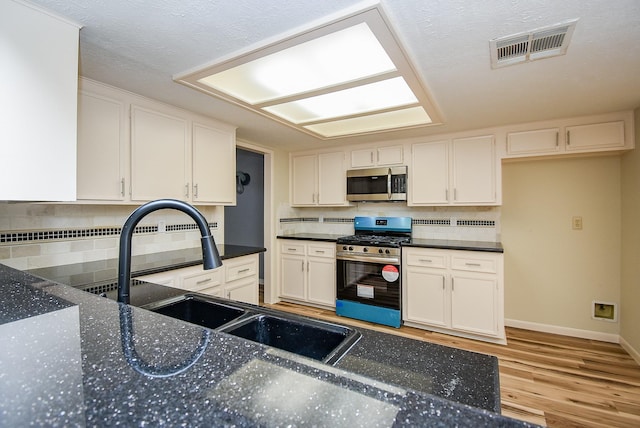 kitchen with white cabinets, sink, light hardwood / wood-style flooring, tasteful backsplash, and stainless steel appliances