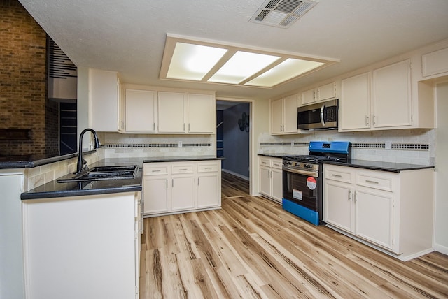 kitchen with gas range, white cabinetry, sink, light hardwood / wood-style floors, and decorative backsplash