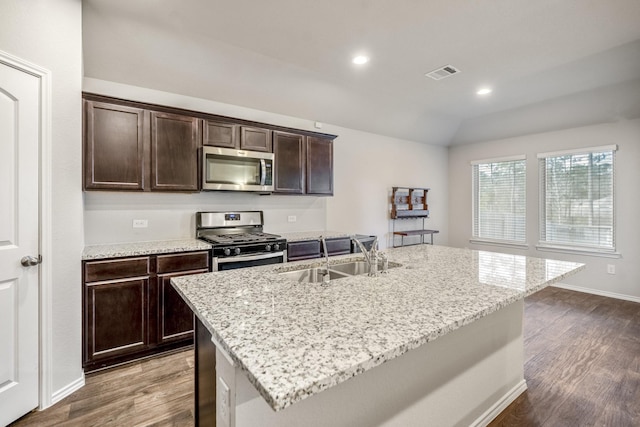 kitchen with dark brown cabinetry, a kitchen island with sink, light stone counters, and appliances with stainless steel finishes