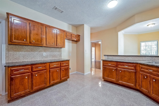 kitchen with decorative backsplash, sink, dark stone counters, and a textured ceiling