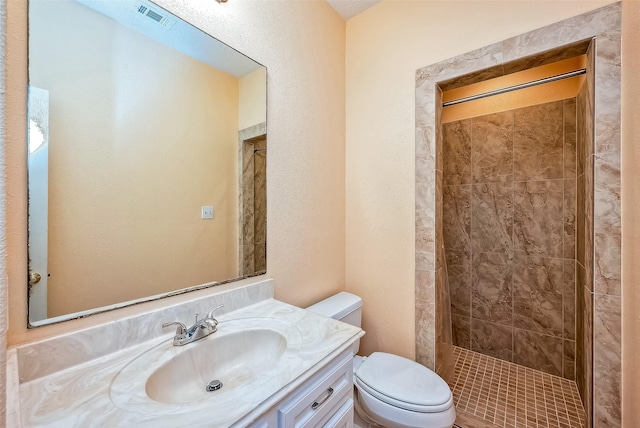 bathroom featuring a tile shower, vanity, and toilet