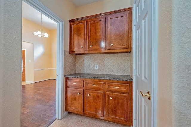 kitchen featuring backsplash, light tile patterned floors, decorative light fixtures, an inviting chandelier, and dark stone countertops