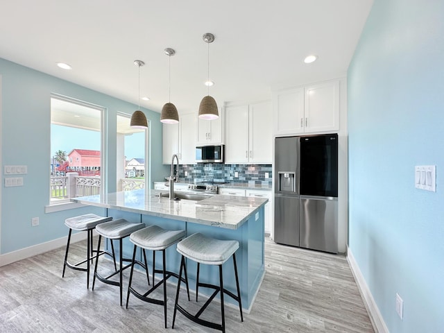 kitchen with white cabinetry, hanging light fixtures, backsplash, a kitchen island with sink, and appliances with stainless steel finishes