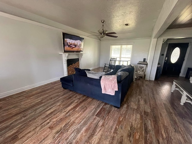 living room with ceiling fan, crown molding, dark wood-type flooring, and a textured ceiling