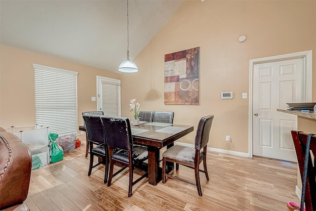 dining room with high vaulted ceiling and light hardwood / wood-style floors