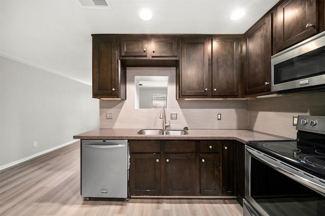 kitchen with light stone countertops, appliances with stainless steel finishes, light wood-type flooring, dark brown cabinets, and sink