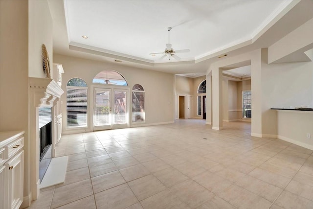 unfurnished living room with a tray ceiling, ceiling fan, crown molding, and light tile patterned floors